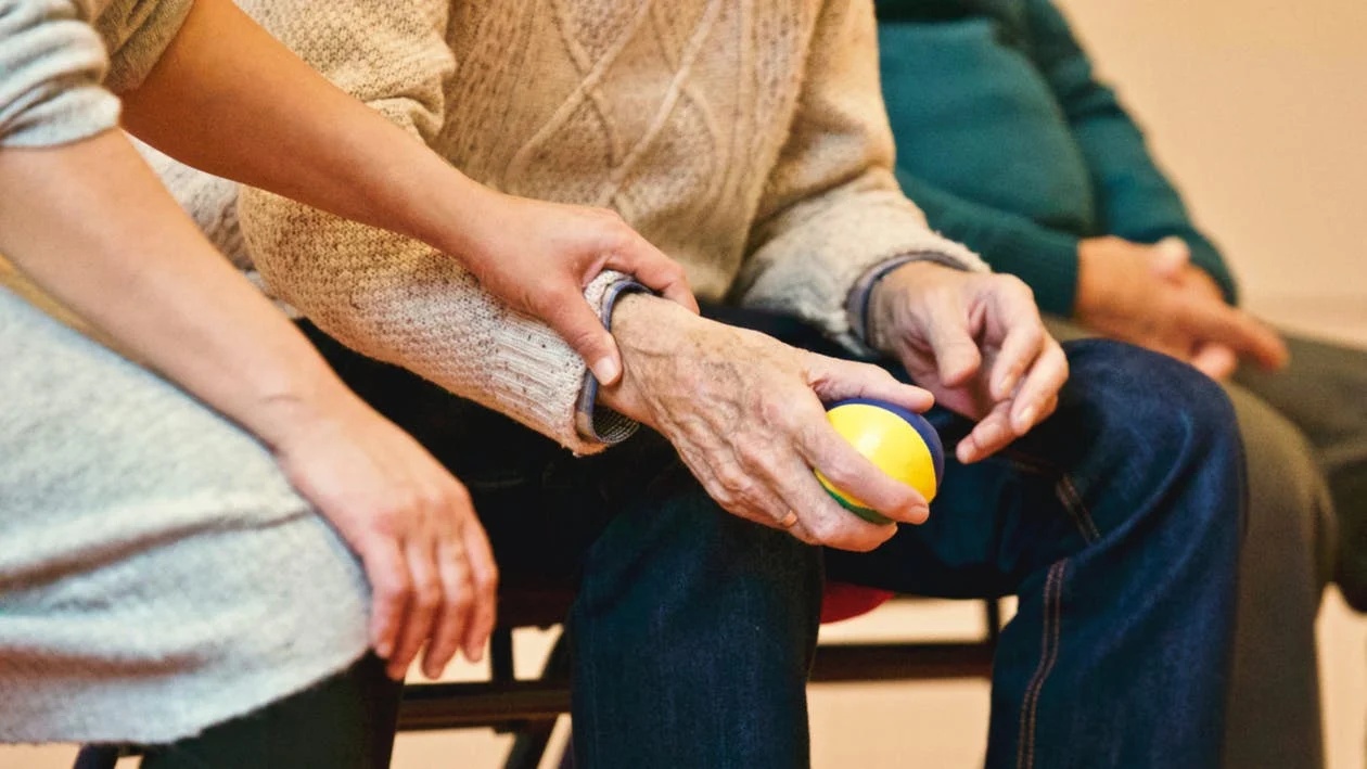 Picture of an old person holding a stress ball with someone holding their hand